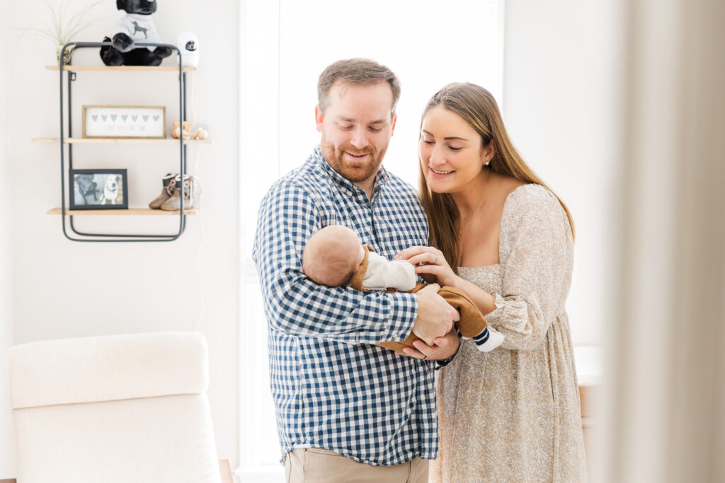 clayton newborn photographer husband and wife standing hold their newborn while talking to him 