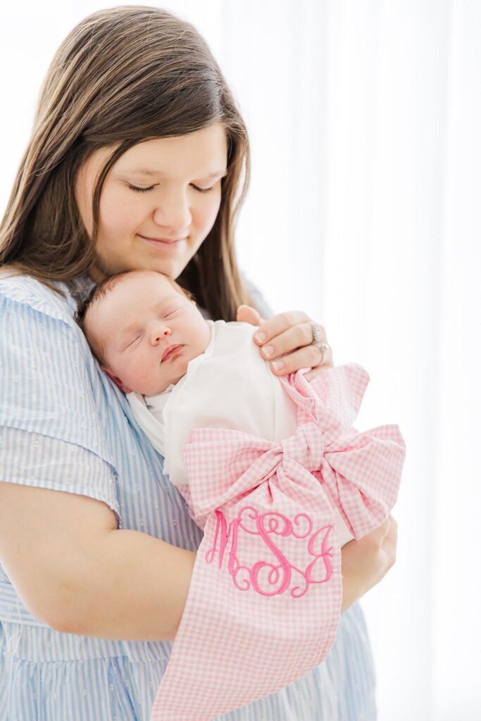 Soft portrait of a mother holding her sleeping baby girl in a timeless studio session with an Apex newborn photographer.