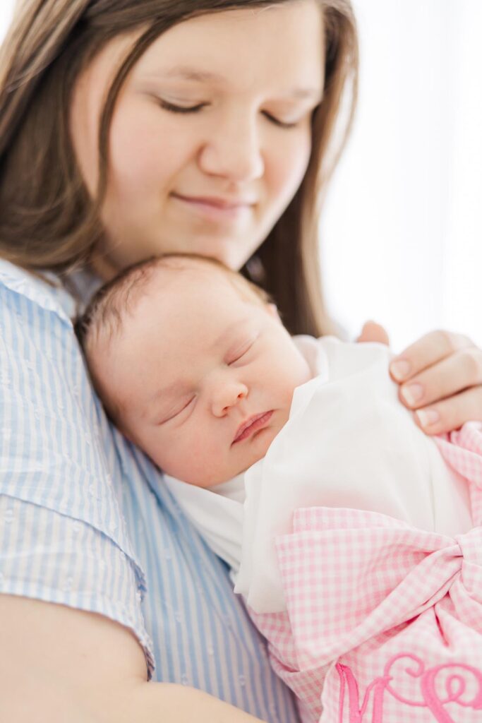 Mother holding her sleeping newborn daughter wrapped in a white swaddle during a light and airy studio session with an Apex newborn photographer.