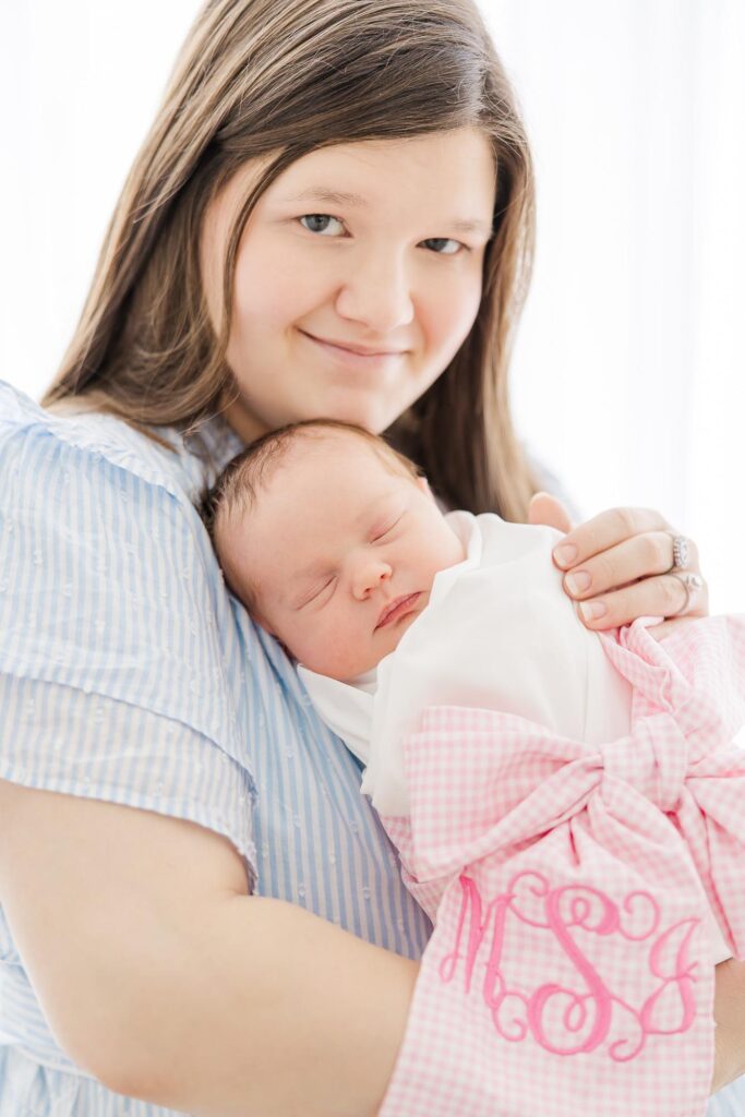 Mother cuddling her newborn daughter wrapped in pink during a bright studio session with an Apex newborn photographer.