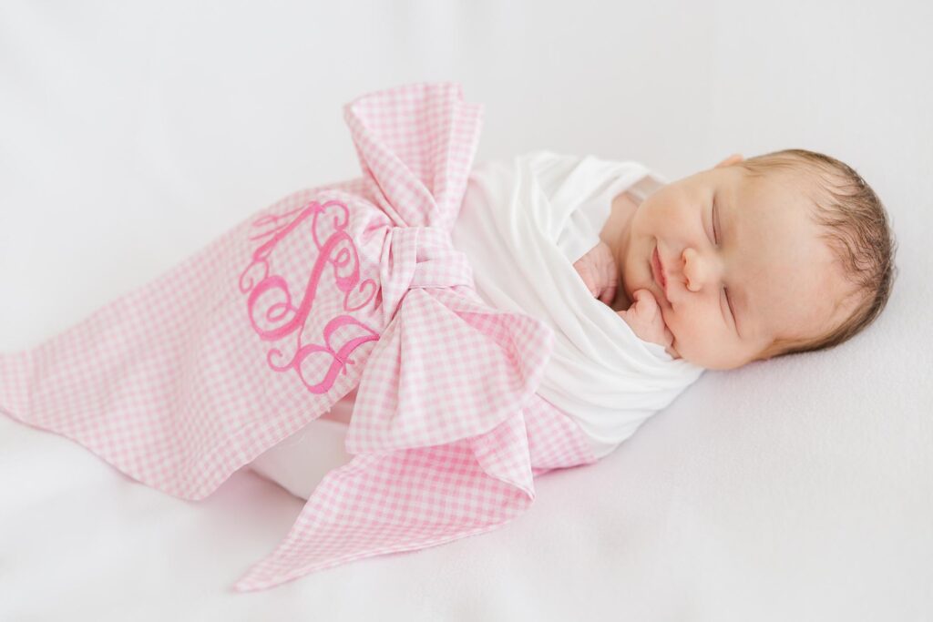 Close-up detail of a newborn girl wrapped in a pink gingham bow blanket, photographed by an Apex newborn photographer.