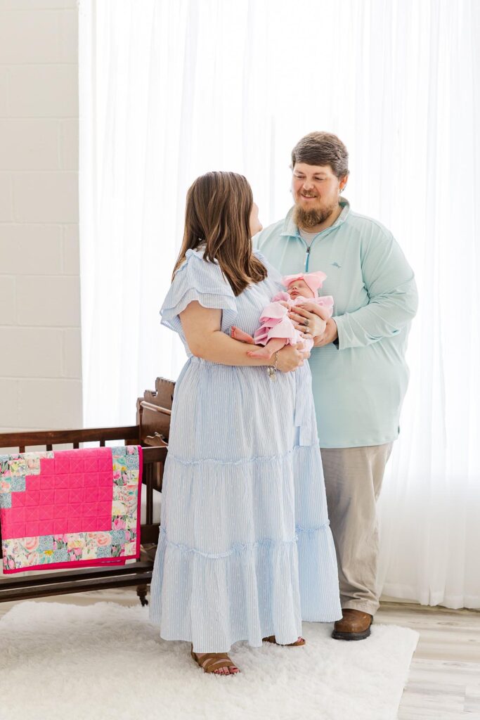 Wife and husband looking at each other holding their baby in front of large window