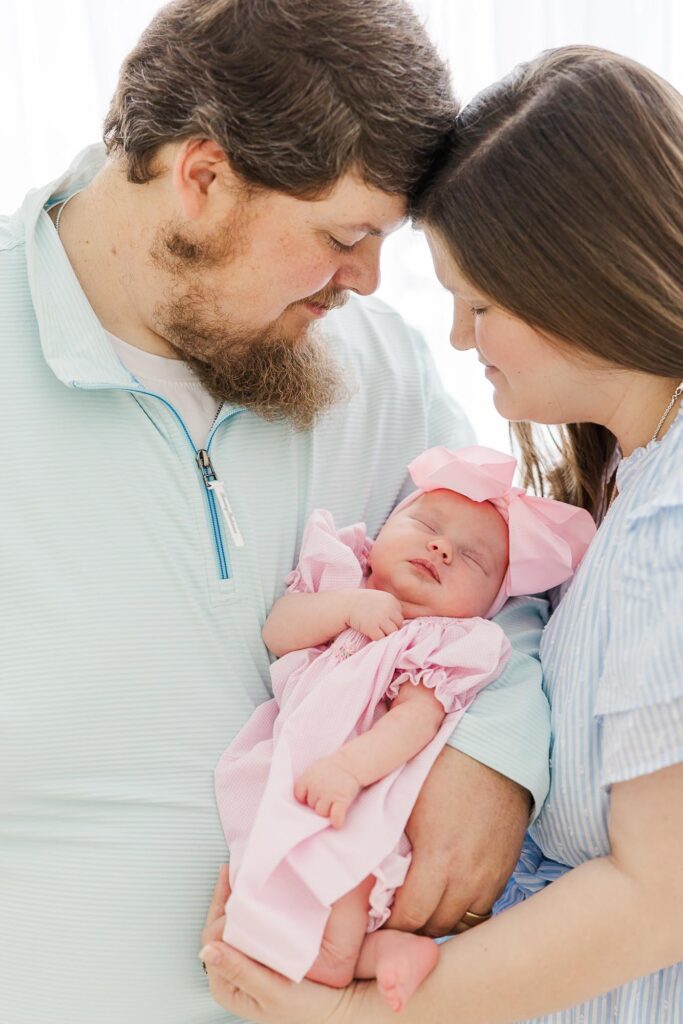 Mother and father holding their newborn baby girl wrapped in pink during a light and airy session with an Apex newborn photographer.