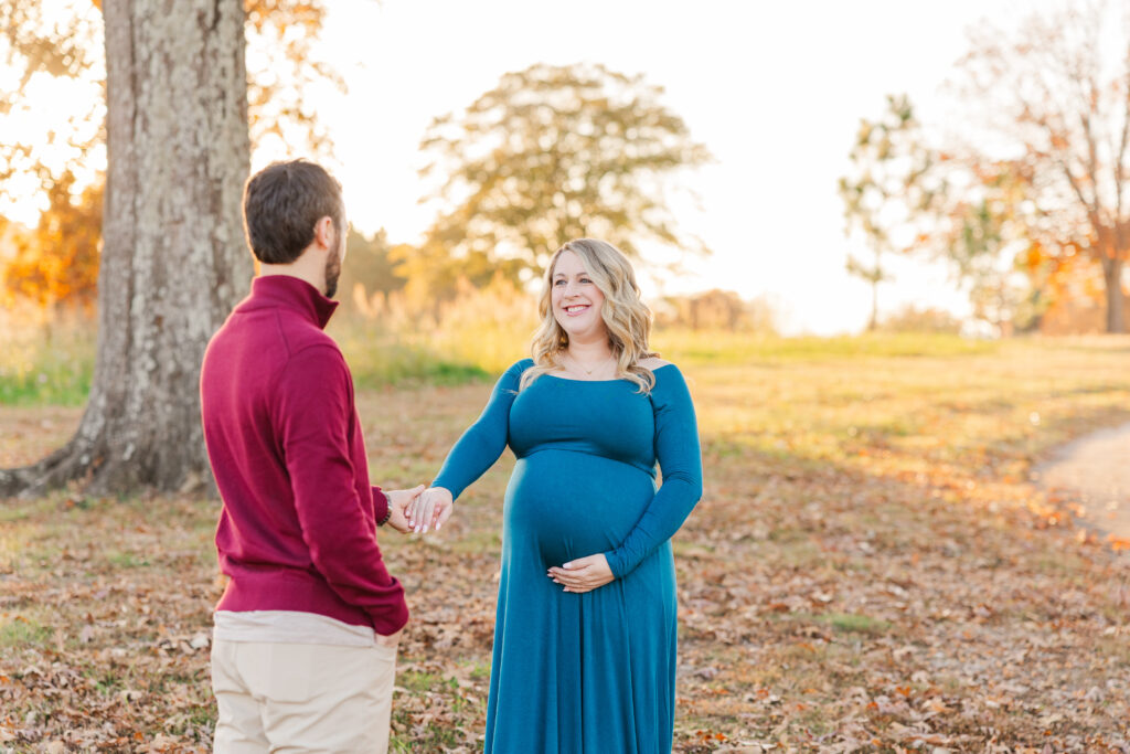 Mother holding her pregnant bump next to the father in blue dress while posing for their clayton maternity photographer