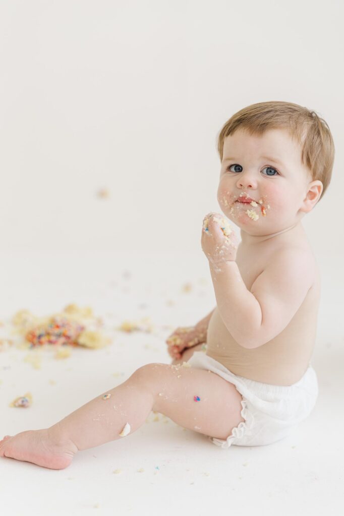 Baby smiling with frosting on face during first birthday cake smash session | Raleigh cake smash photographer