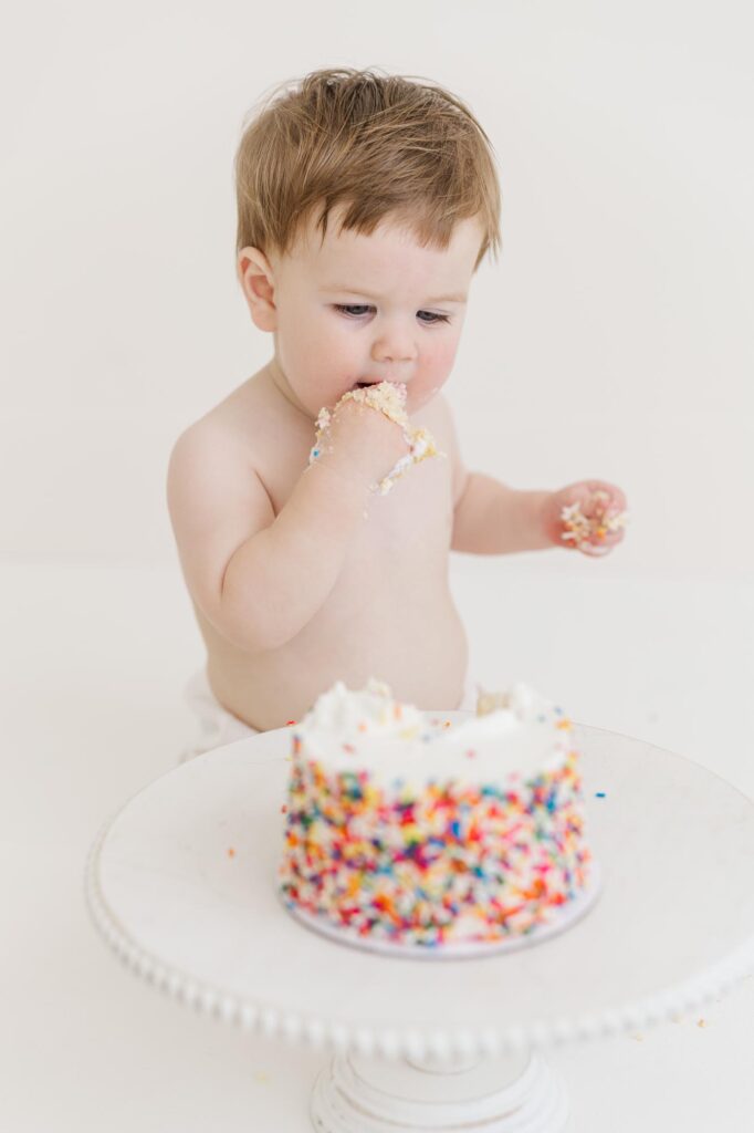 Baby enjoying cake during first birthday cake smash session in white studio setup | Raleigh cake smash photographer
