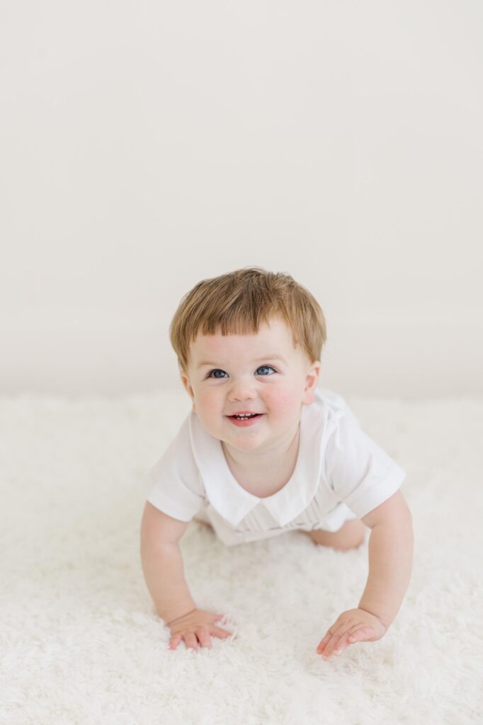 Baby boy crawling on white studio floor during personality portraits before cake smash session | Raleigh cake smash photographer