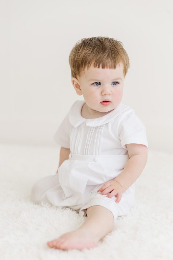 Baby boy sitting on white backdrop during first birthday personality portraits | Raleigh cake smash photographer