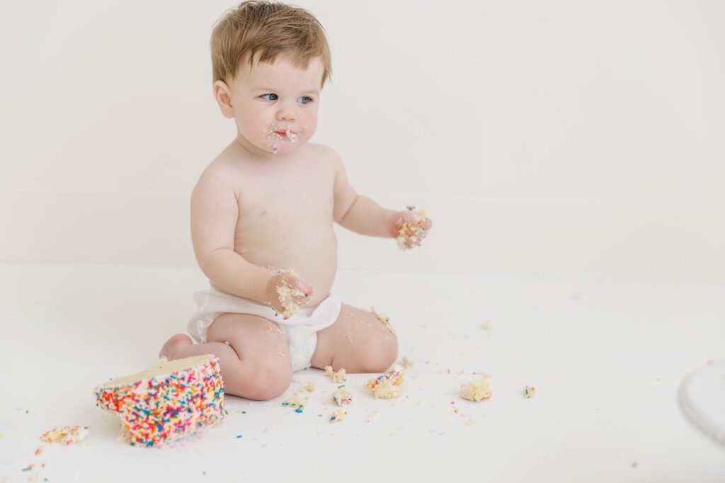 Baby sitting with sprinkle cake during first birthday cake smash photography session near Raleigh NC