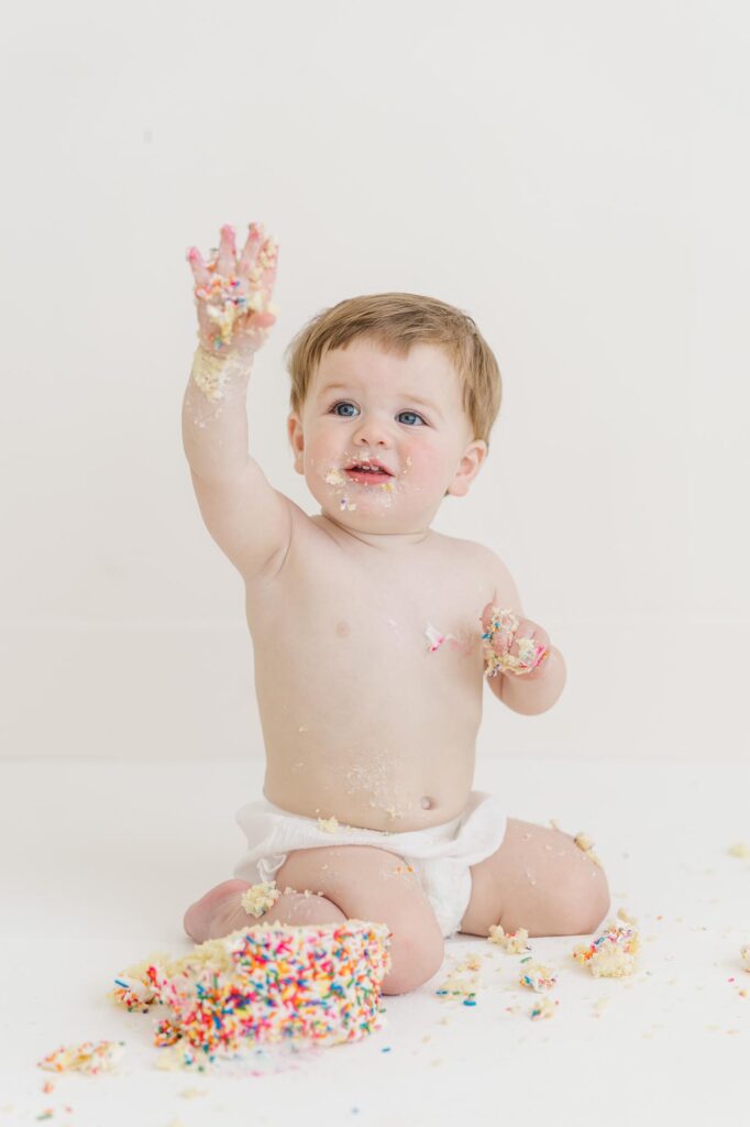 One year old baby throwing cake during fun studio cake smash session | Raleigh cake smash photographer