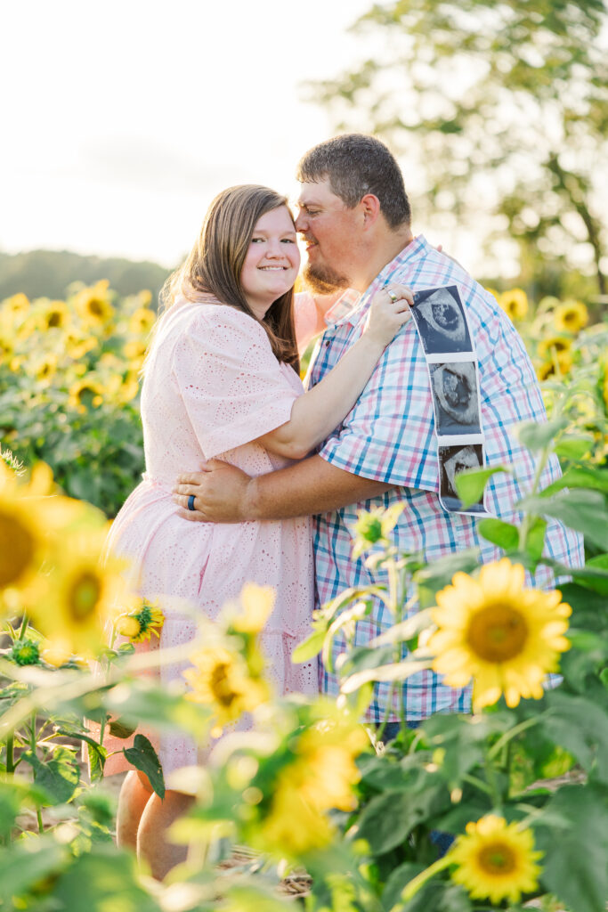Expecting couple embracing in a sunflower field during sunset at one of the most beautiful Raleigh photography locations.