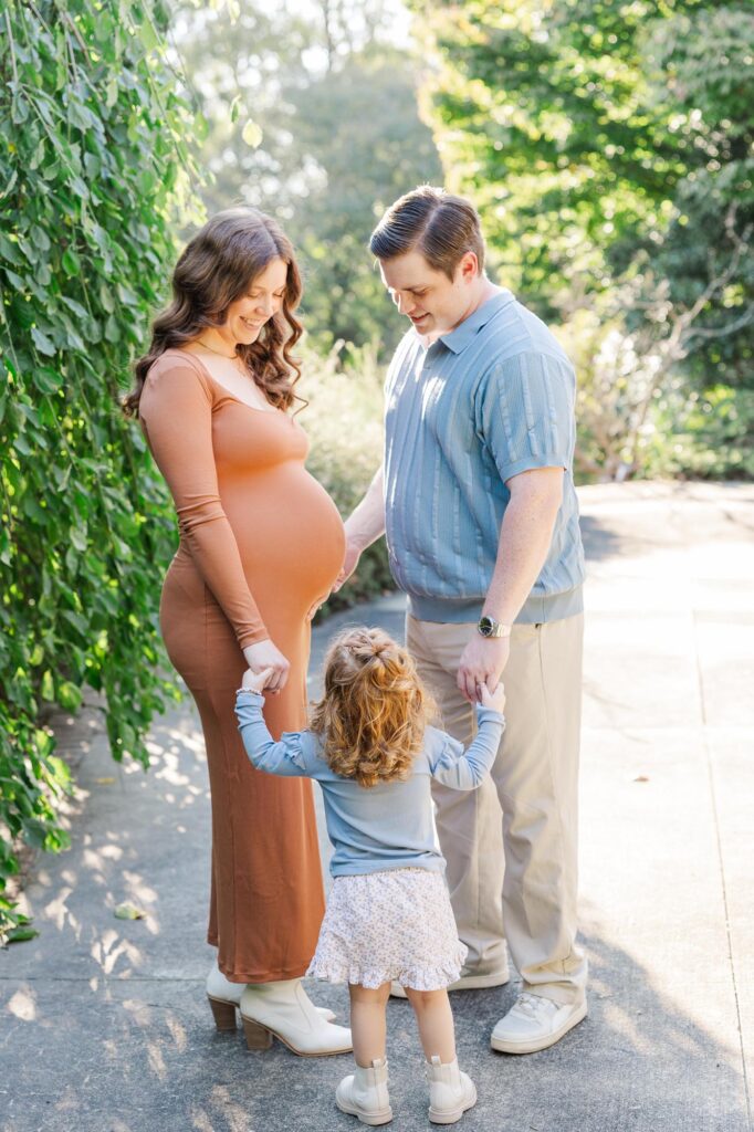 Expecting mother with toddler holding hands during a maternity session at a scenic Raleigh photography location.