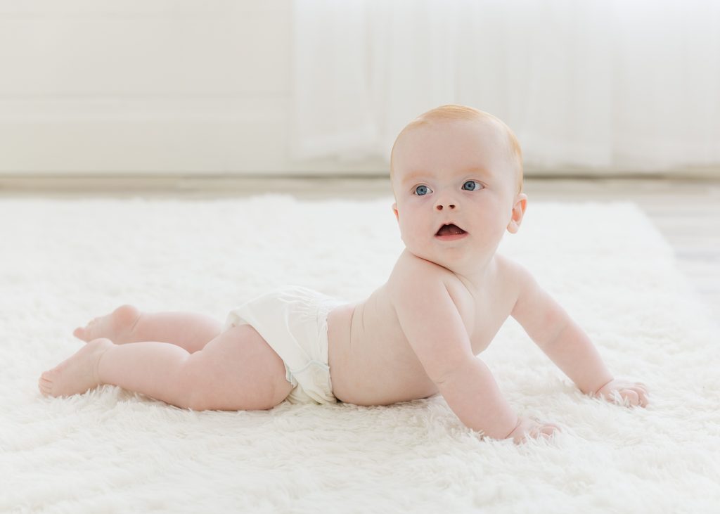 Baby laying on a white carpet in a bright and airy photography studio for his six month photos